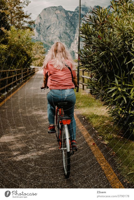 Young woman rides a bicycle on Lake Garda northern italy Torbole Bicycle Wheel cycle path Mountain vacation travel Movement jeans free time Summer Sun