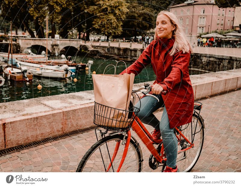 Junge Frau fährt mit dem Fahrrad durch Riva del Garda gardasee norditalien fahrrad stadt mobilität bewegung shopping einkaufen hafen regen sommer regenjacke