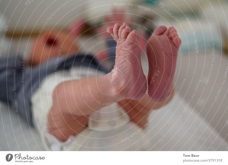 Close-up of the baby's feet while the baby is lying on the changing table and stretching his feet in the air in the blurred background you can see that the baby is crying