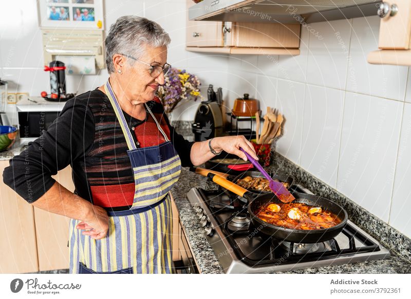 Mature woman cooking fish dish at home stew sauce prepare food process kitchen seafood cod housewife culinary stove pan recipe female lifestyle household