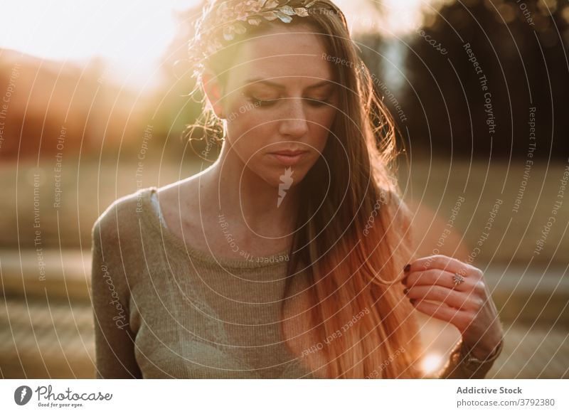 Crop calm attractive woman standing in nature in evening sun charming serene peaceful tranquil gorgeous unemotional park sunbeam gentle tender sensitive trendy