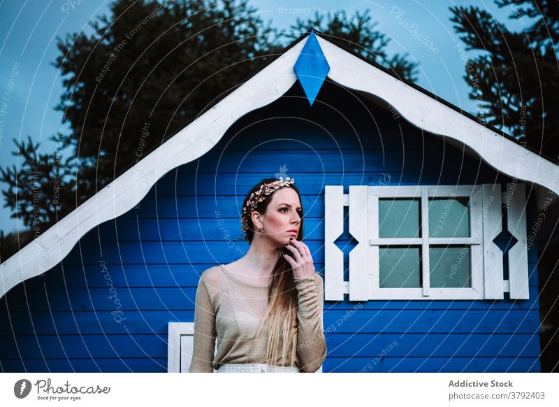 Attractive woman standing near small blue house confident cool style appearance trendy park calm construction emotionless tranquil gorgeous serene elegant