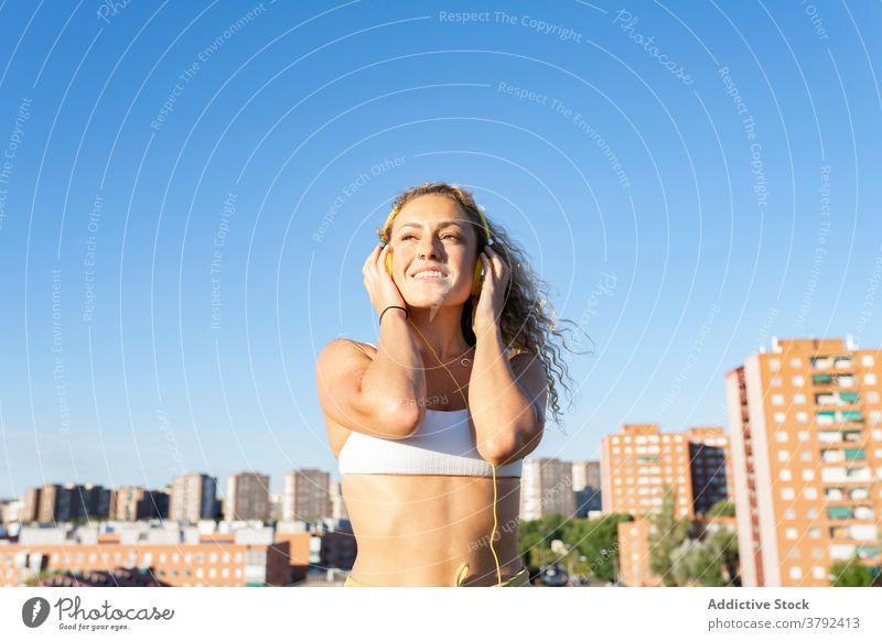 Positive woman in sports bra listening music via headphones positive optimistic enjoy sound entertain gadget cheerful sunny summer young melody song slim