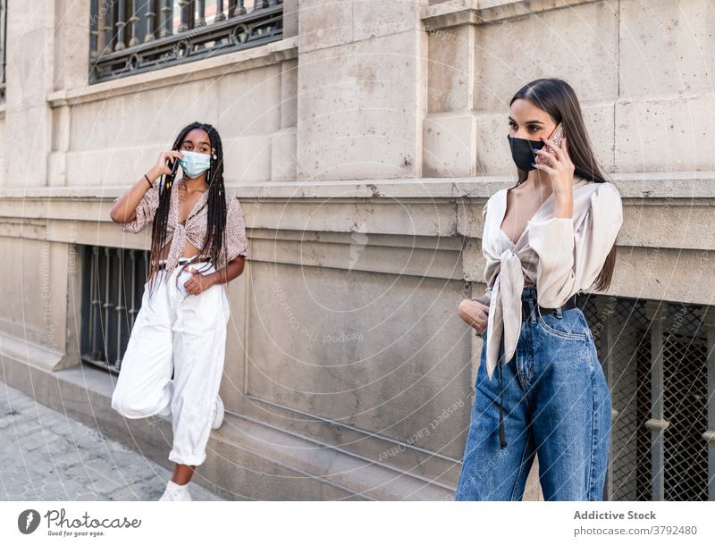 Stylish diverse women in masks talking on smartphones in city speak together street style protect coronavirus covid 19 multiethnic multiracial black