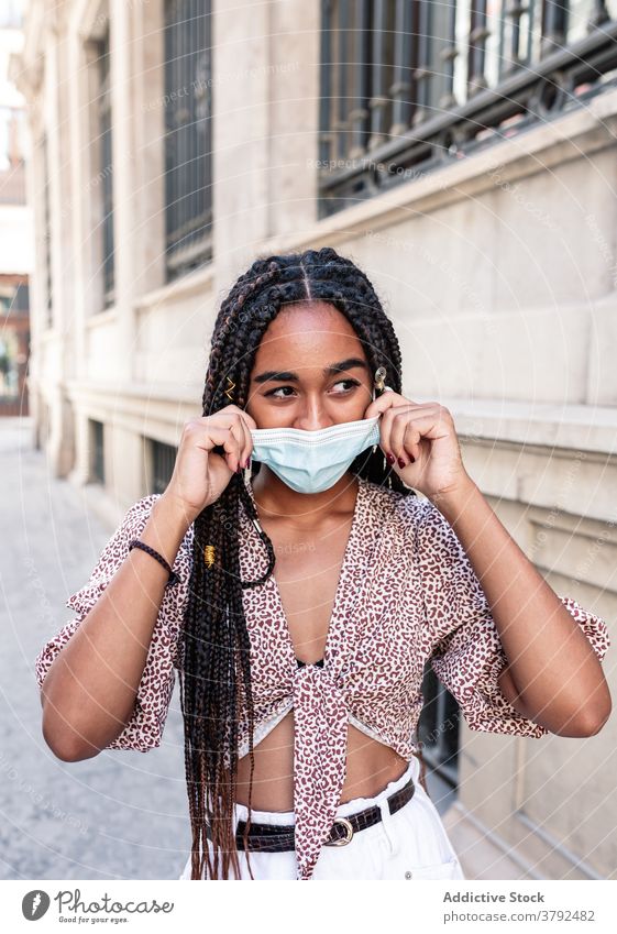 Stylish ethnic woman in medical mask on street style put on adjust city outbreak covid 19 female black african american braid hairstyle outfit trendy urban