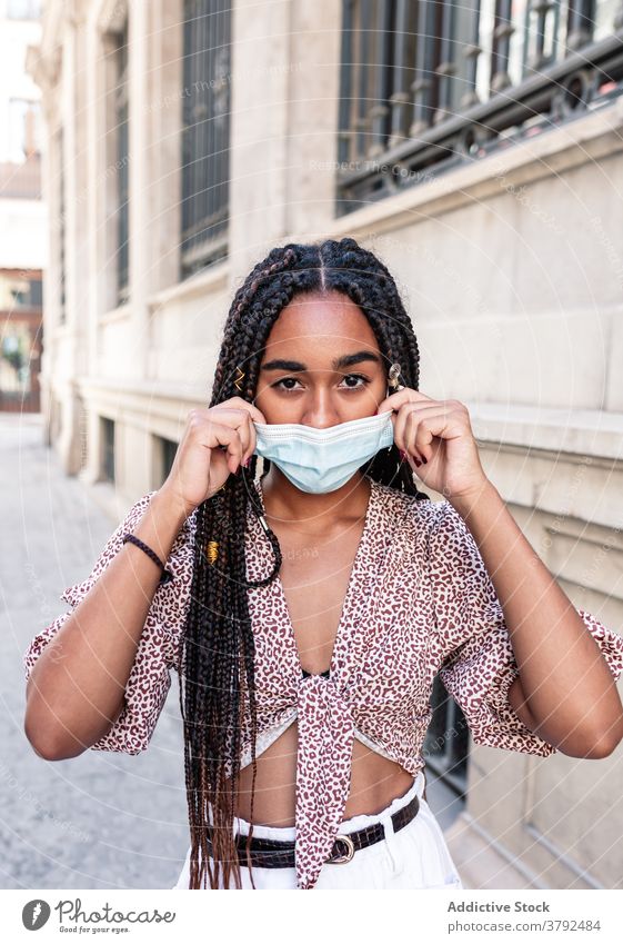 Stylish ethnic woman in medical mask on street style put on adjust city outbreak covid 19 female black african american braid hairstyle outfit trendy urban