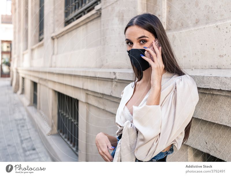 Trendy woman in mask talking on mobile phone on street smartphone coronavirus protect using speak style female stone building city conversation connection urban