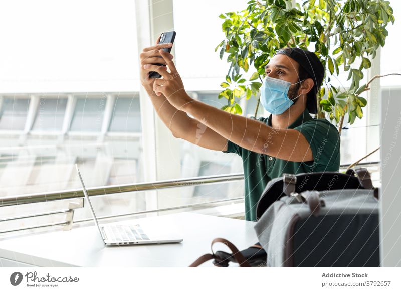 Man in protective mask taking selfie on smartphone self portrait man medical coronavirus prevent using smile male laptop photo table cheerful sit happy online