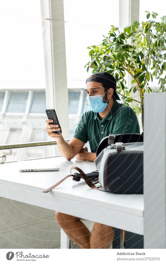Man in protective mask using smartphone man medical coronavirus prevent smile male laptop photo table cheerful sit happy online device cellphone gadget guy