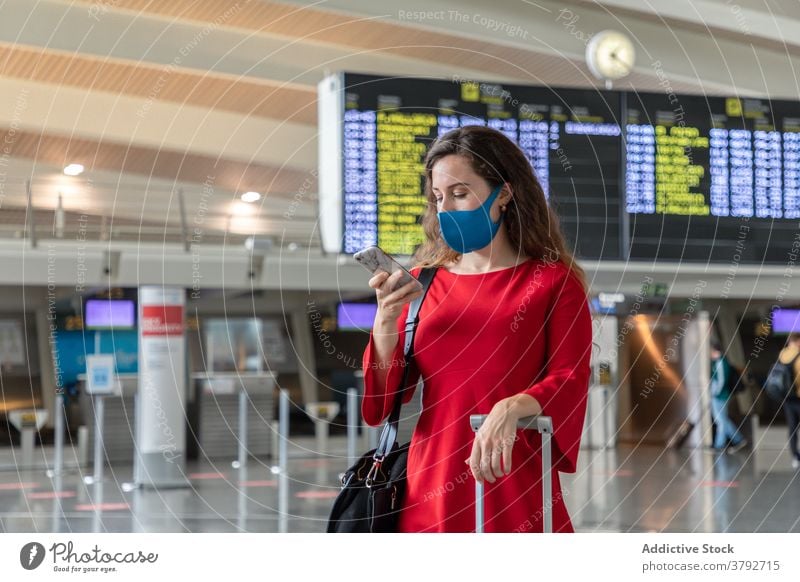 Woman in mask using smartphone in airport woman departure board wait flight traveler female coronavirus suitcase vacation luggage browsing cellphone baggage