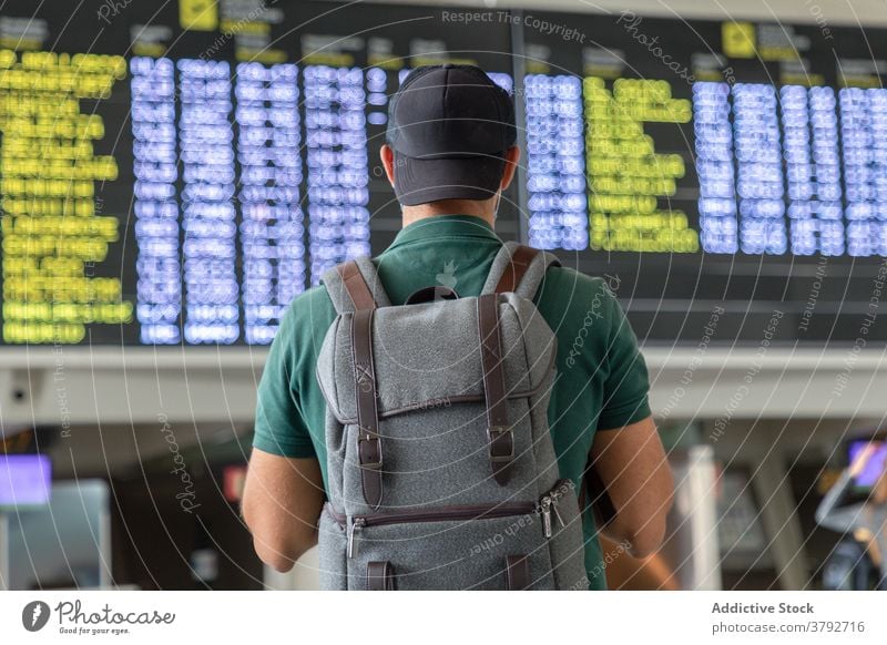 Unrecognizable man with backpack in airport departure board schedule traveler check wait flight tourist male international vacation trip passenger modern