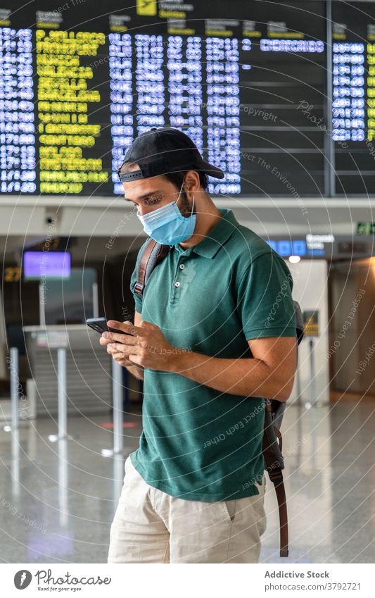 Traveler in mask using cellphone in airport wait flight man departure terminal board smartphone male covid 19 passenger modern browsing tourist gadget device