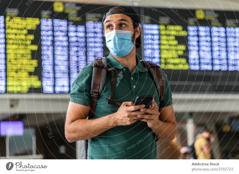 Traveler in mask using cellphone in airport wait flight man departure terminal board smartphone male covid 19 passenger modern browsing tourist gadget device