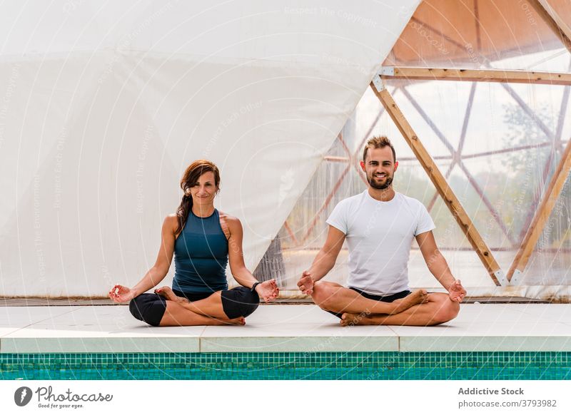 Couple sitting in Lotus pose while reflecting in swimming pool couple lotus pose yoga practice reflection wellbeing spirit stress relief wellness tent asana