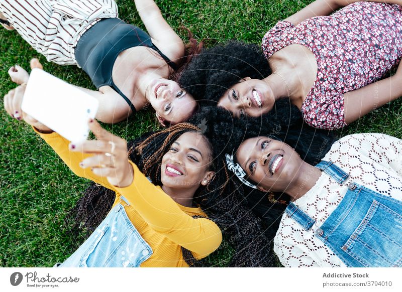 Delighted multiethnic female friends taking selfie on grass women together company friendship smartphone self portrait cheerful having fun multiracial diverse