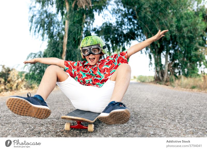 Happy boy on skateboard in protective eyeglasses helmet goggles having fun carefree childhood excited content road stylish apparel decorative summer trendy