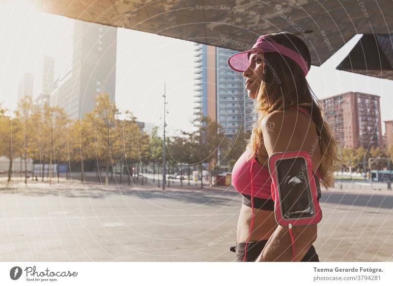 Girl listening to music on her armband with touchscreen and headphones in Barcelona activewear adult athletic girl running runner exercise cardio fitness woman