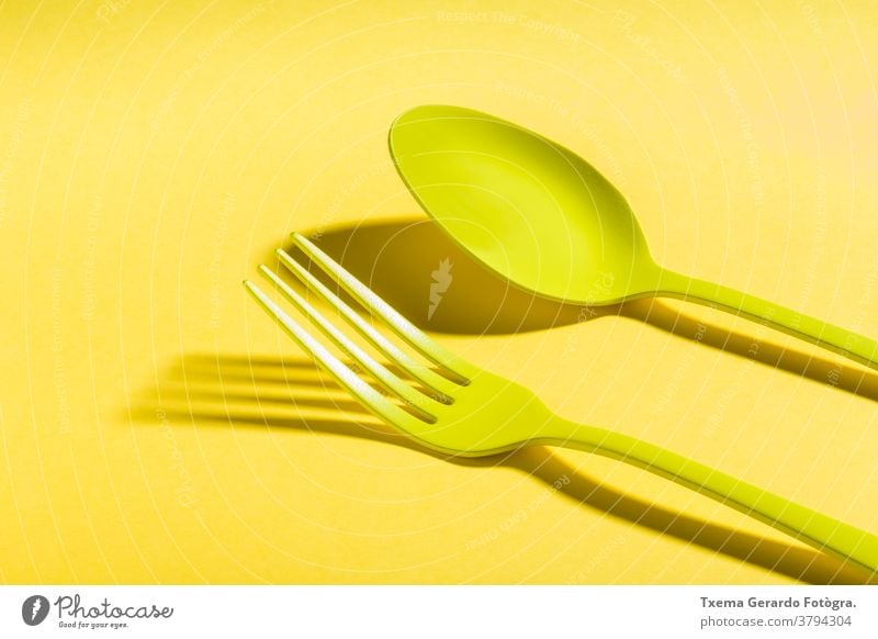 Set of yellow cutlery casting a shadow on yellow background spoon fork saturated color isolated surreal concept silverware food top view still life minimalist