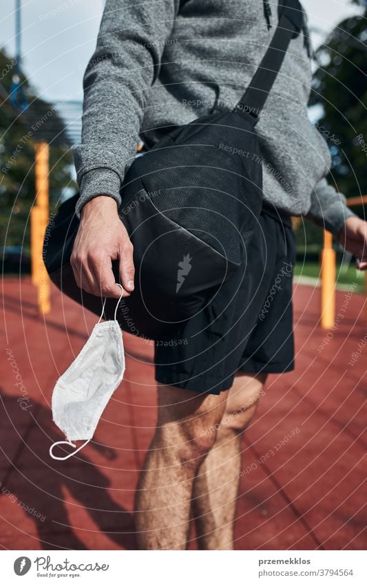 Young man standing in street workout calisthenics park holding the face mask need to avoid virus infection bag boy care caucasian contagious corona coronavirus