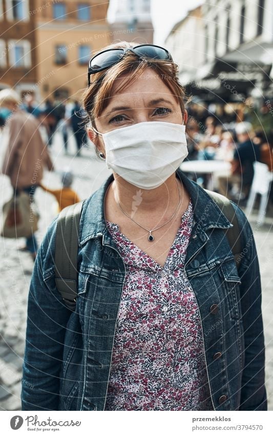 Young woman standing in a street downtown looking at camera wearing the face mask to avoid virus infection care caucasian contagious corona coronavirus cover