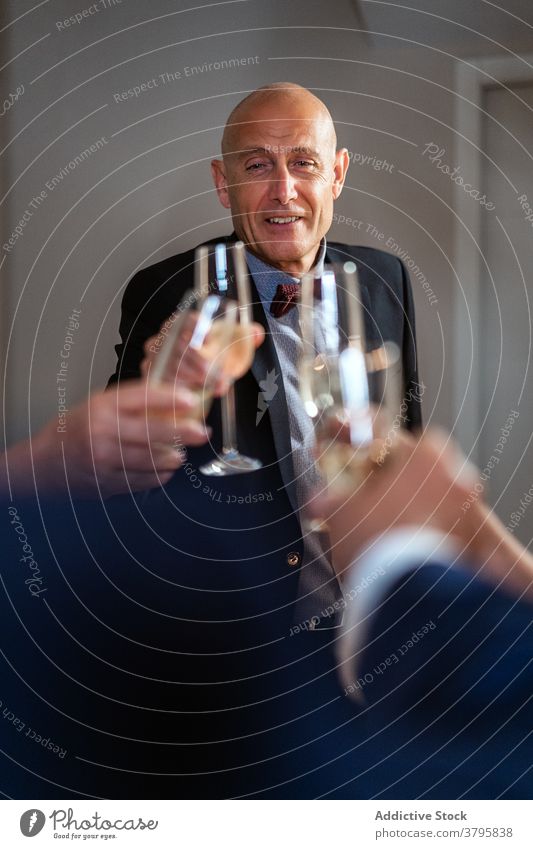 Smiling man clinking glasses with friends during party champagne christmas people celebrate holiday drink festive together suit classy mature alcohol gather