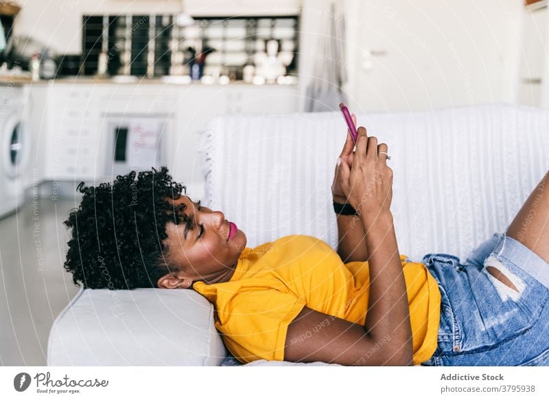 Laughing black woman using smartphone at home laugh having fun excited browsing mobile cheerful millennial young adolescent female modern device gadget