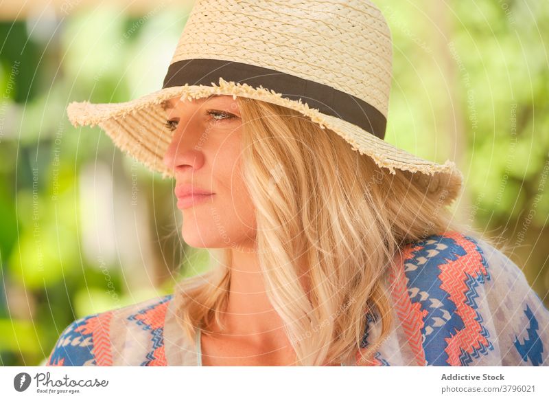 Pensive young woman in straw hat looking away in sunlight dreamy relax holiday summer style fashion rest traveler nature green garden female blond trendy