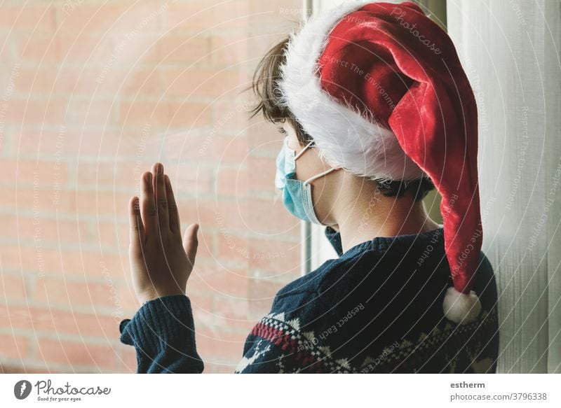 kid with medical mask wearing Santa Claus hat wait for santa claus next to a window in Christmas child christmas coronavirus Christmas Eve 2019-ncov epidemic