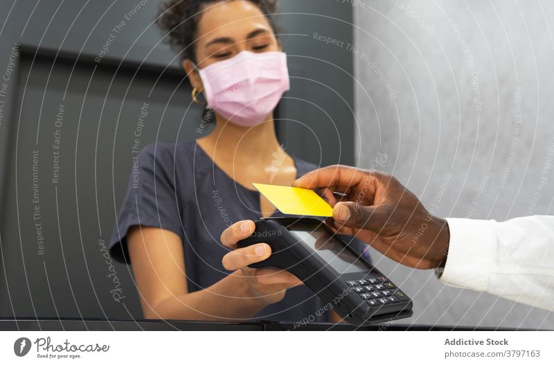 Crop man using terminal for payment in clinic pos contactless patient reception purchase medicine plastic card ethnic black african american medical mask