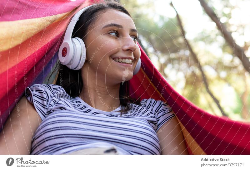 Carefree woman listening to music in hammock enjoy hang park wireless melody calm headphones peaceful sound lying serene song harmony audio modern relax rest