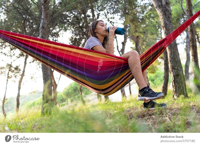 Calm woman drinking water in hammock thirst hydrate park bottle refreshment hang female summer beverage enjoy rest relax recreation nature healthy young lady