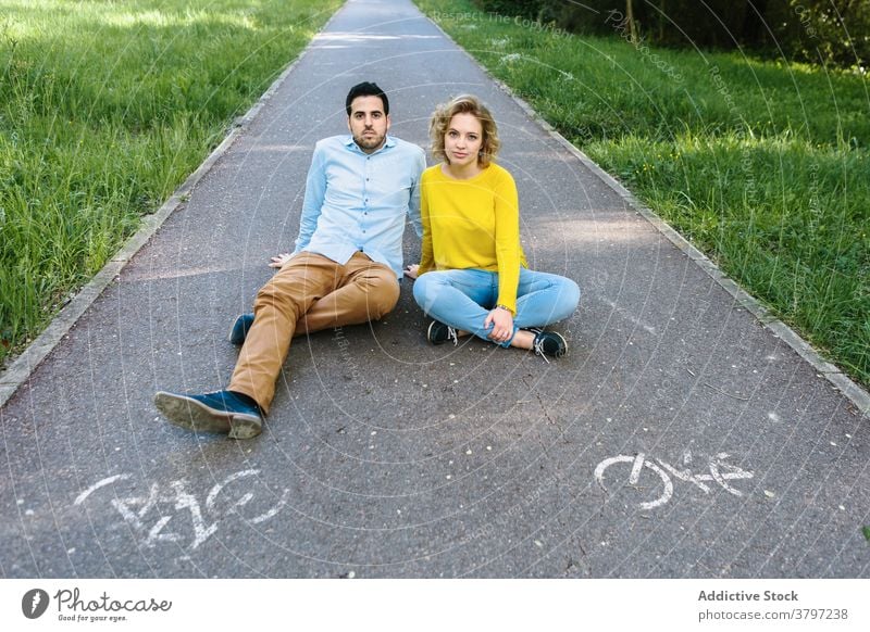 Carefree couple on asphalt road in park carefree relationship relax walkway summer trendy green outfit together sit calm love urban enjoy young rest style