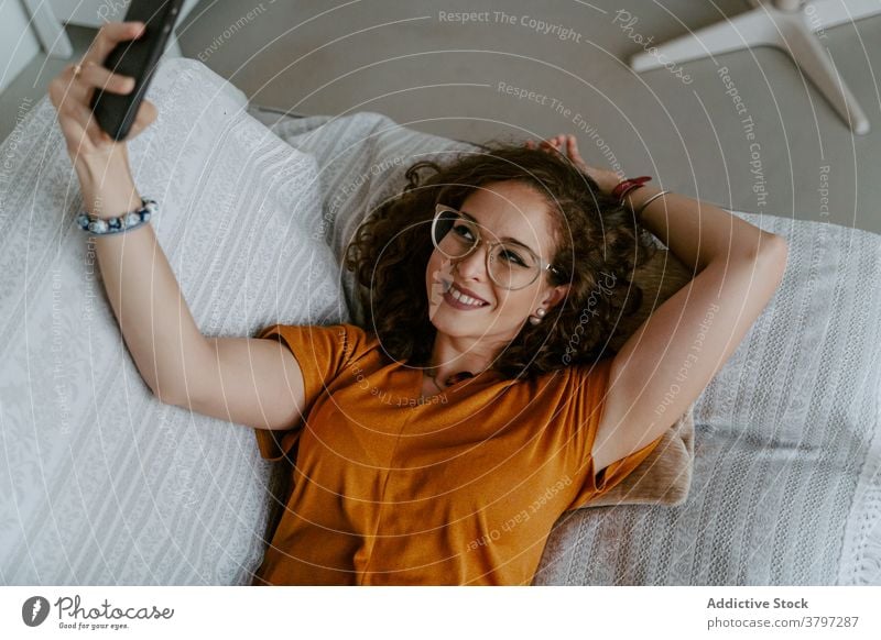 Young female taking self portrait on smartphone lying on sofa woman selfie relax social media comfort using gadget home device lazy young casual ginger hair
