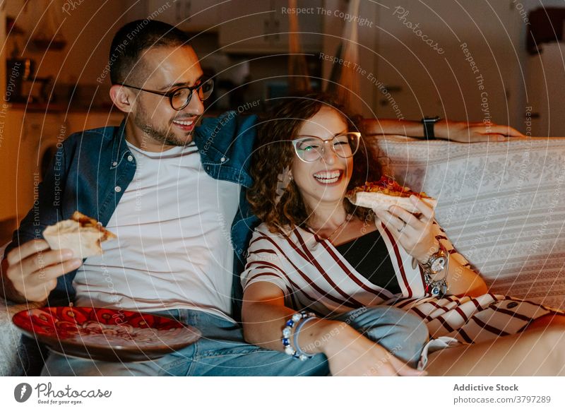 Young couple watching film on laptop and eating pizza at home movie cuddle entertain love romantic relax couch together relationship boyfriend girlfriend young