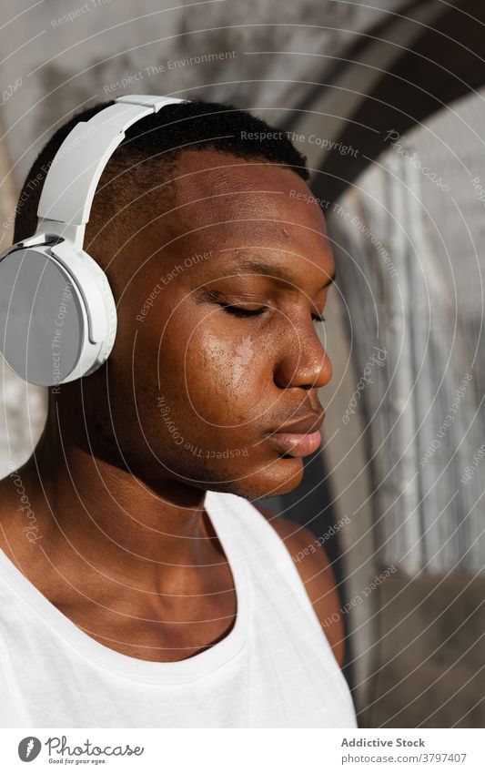 Black serious man listening to music in headphones calm eyes closed relax song athlete wireless sound male rest audio melody wellness tune concentrate wellbeing