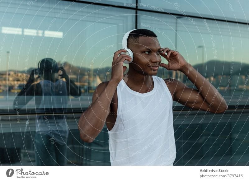 Cheerful black man listening to music in headphones cheerful joy sound athlete wireless optimist male training device gadget smile melody song guy tune rest