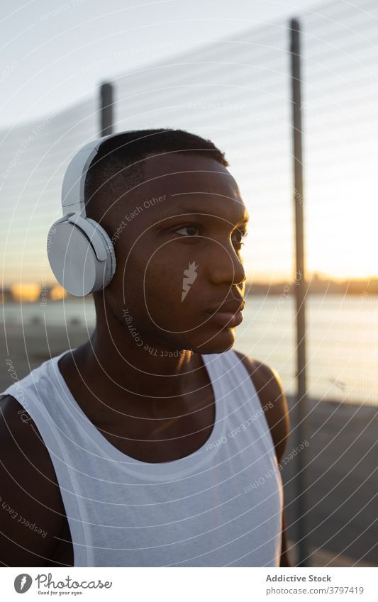 Black sportsman in headphones resting after training athlete serious muscular sporty music listen fit male sportswear lifestyle wellbeing device activity