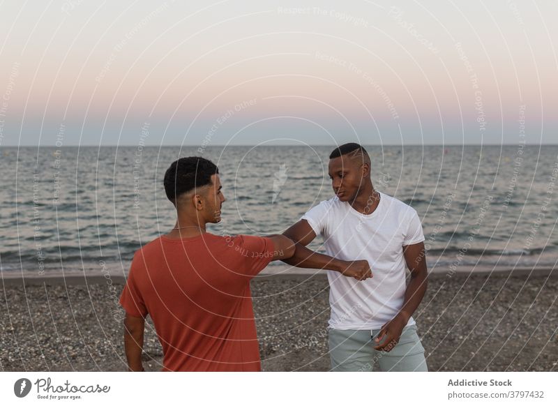 Stylish black friends bumping elbows on sea shore in evening greeting stylish haircut ocean beach sky sunset men african american modern style bright partner