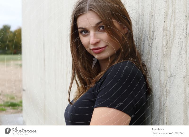 Close, lateral portrait of a young woman in front of a concrete wall Woman Young woman 18-25 years warmly pretty Charming Slim Brunette long hairs Fresh Large