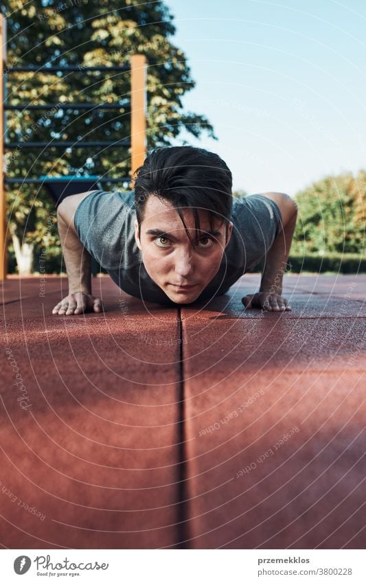 Young man doing push-ups on a red rubber ground during his workout in a modern calisthenics street workout park care caucasian health lifestyle male one
