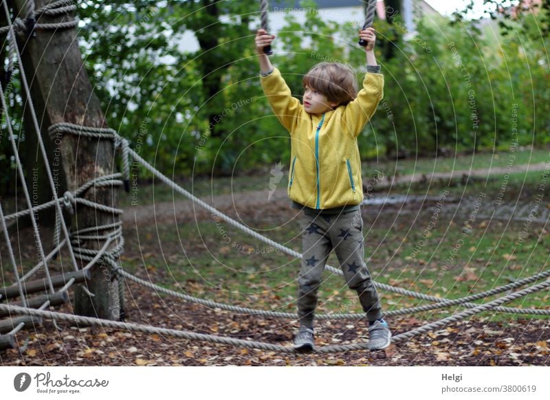 Boy balancing on a rope at a playground in the park Human being Child Boy (child) Rope game device Park balance To hold on Autumn Tree Grass leaves foliage