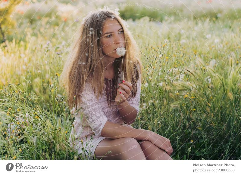 Portrait of a cute caucasian woman sitting on the grass, blowing a dandelion. creative thoughtful blonde field flowers Nature Summer spring Plant Environment