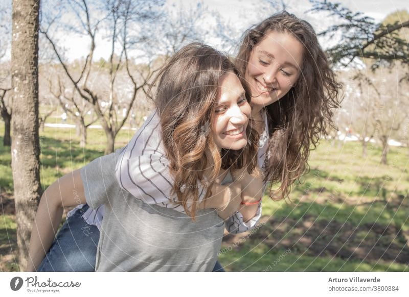 two girls a park of almond trees laughing together, climbed one on top of the other activity background beautiful bright careless cheerful colorful female
