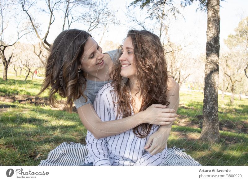 a couple of girls in an almond park looking into each other's eyes, they are sitting on a blanket activity background beautiful bright careless cheerful