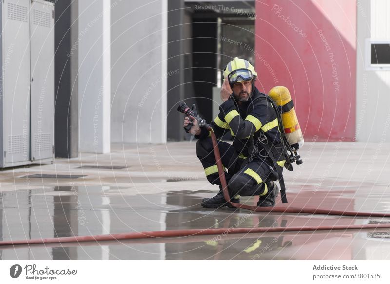 Fireman in uniform on wet pavement near hose firefighter helmet safety profession contemplative reflection equipment glasses wall concrete dreamy fireman