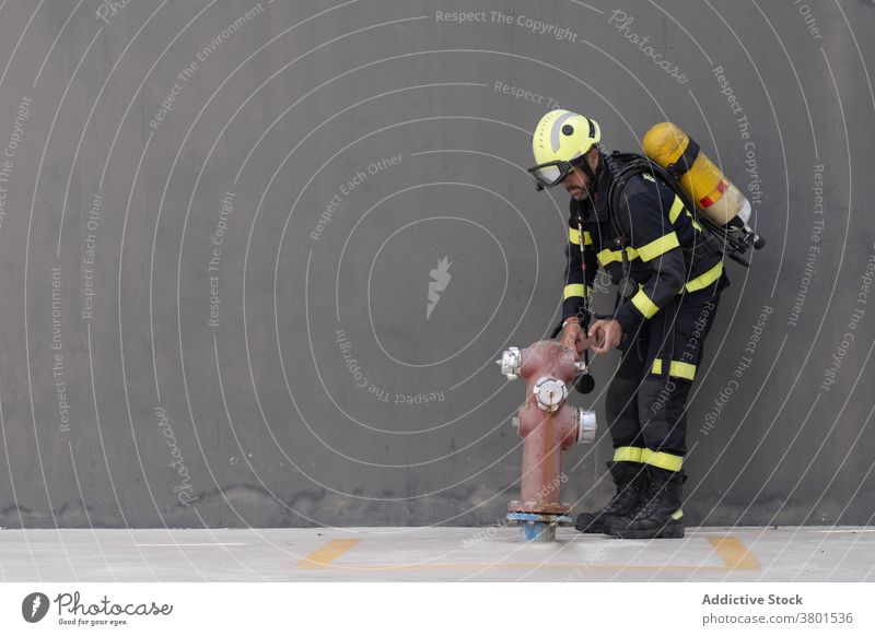 Fireman in uniform with equipment near fire hydrant firefighter profession routine practice extinguisher wall pavement concrete work helmet colorful hardhat
