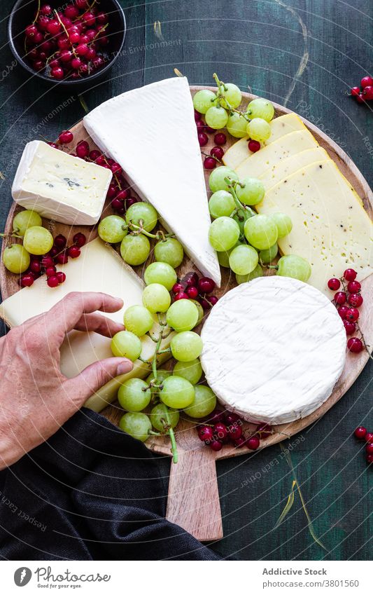 Crop faceless person decorating cheese plate with grapes platter decorate currant dish dessert delicious prepare cuisine appetizing chef serve piece organic