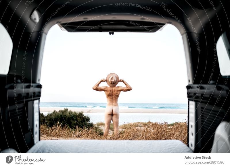 Anonymous naked man outstretching arms in excitement on seashore nude freedom seacoast joy travel excited boot car road trip hat fit bare unclothed stand enjoy
