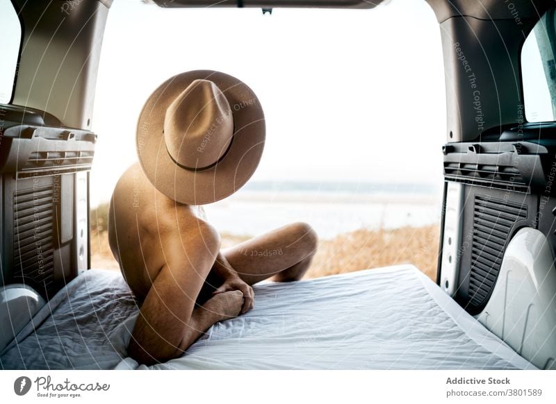 Unrecognizable naked man in hat resting on mattress in vehicle tourist contemplate ocean vacation sky horizon endless felt nude travel transport journey sit