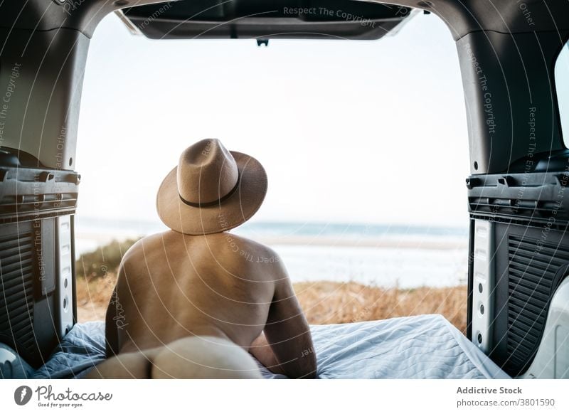 Unrecognizable naked man in hat resting on mattress in vehicle tourist contemplate ocean vacation sky lying horizon endless felt nude travel transport journey